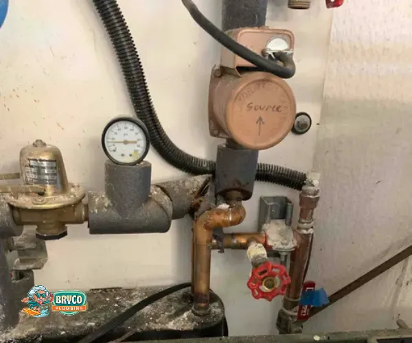 Section of copper plumbing with significant limescale buildup on threaded connections and valves.