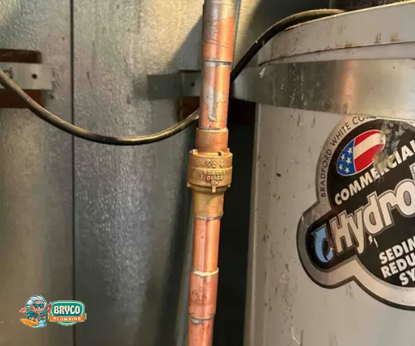 Section of copper plumbing with significant limescale buildup on threaded connections and valves.